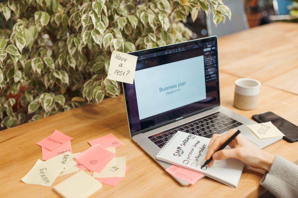 Persona organiza sus tareas y prioridades del día en una libreta junto a su laptop, con notas adhesivas como apoyo visual